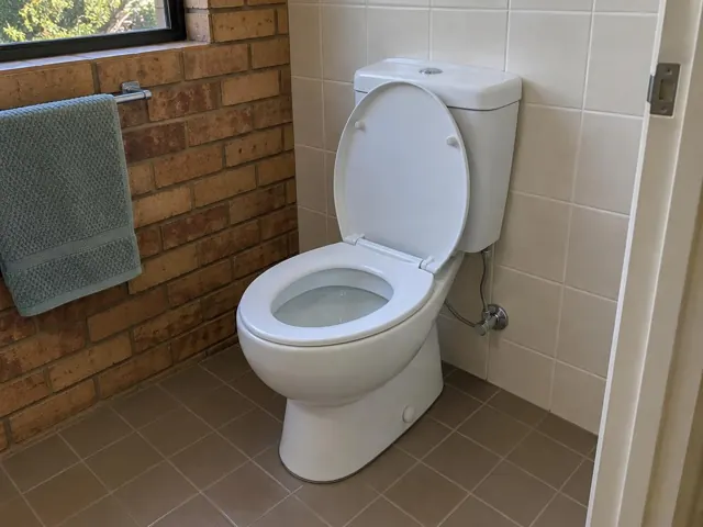 Clean white toilet in a tiled bathroom with brick wall and towel rail in Kings Park