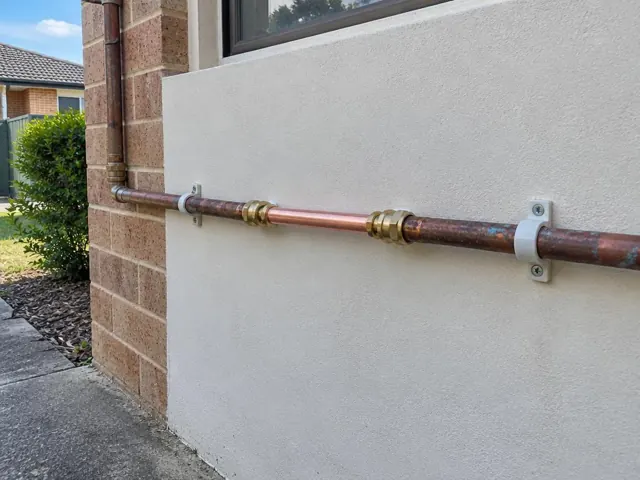 Exterior copper water pipe repair on a rendered brick house wall beside a window in Quakers Hill