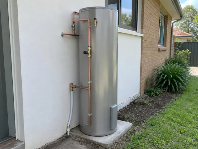 Outdoor hot water cylinder beside a brick house wall and garden in Kings Park
