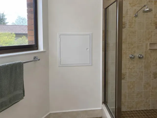 Bathroom wall with a small access panel beside a tiled shower and window in Blacktown