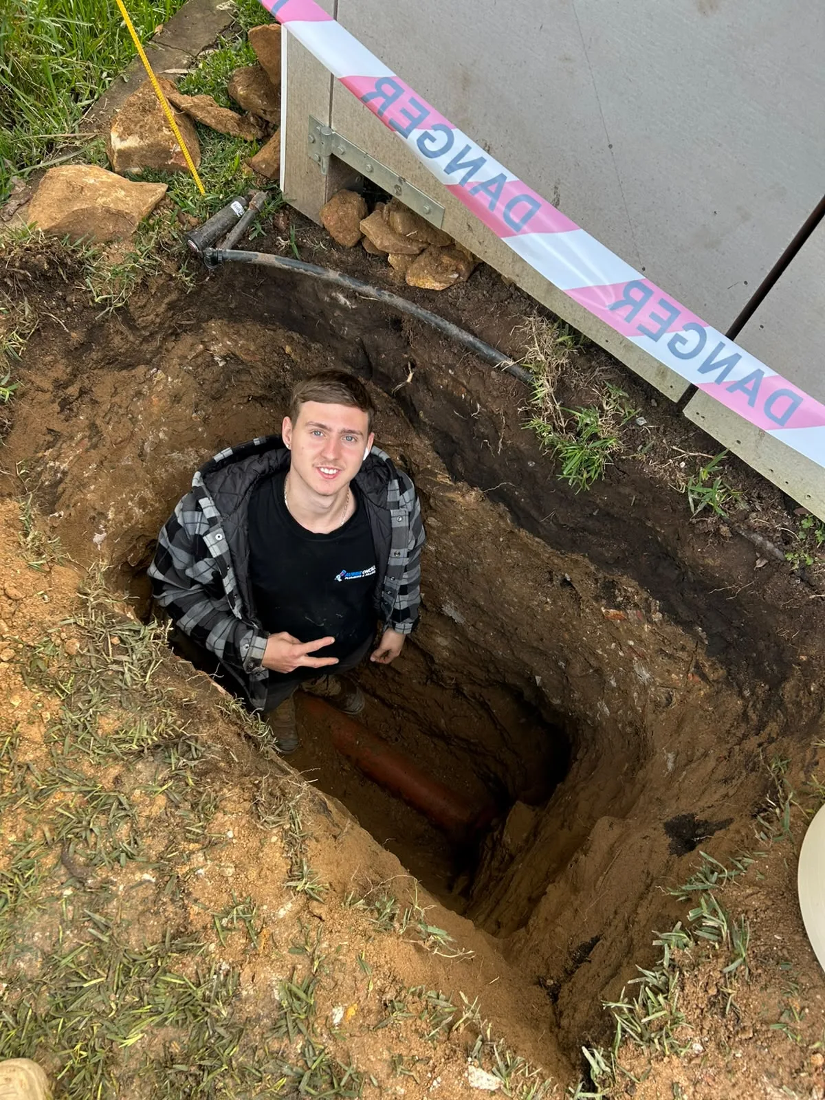 A plumber working in a dug excavation to reach a blocked drain