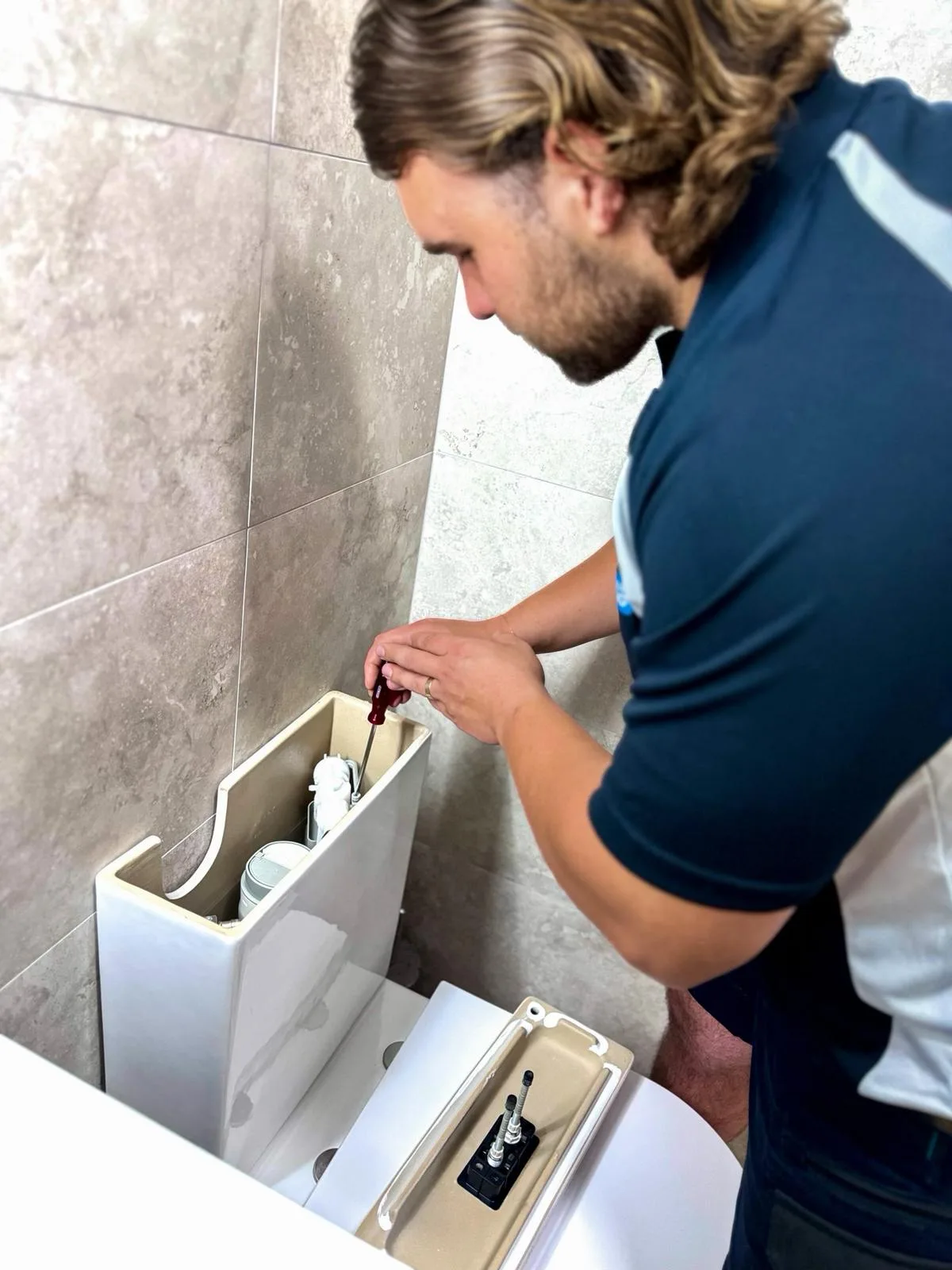 A plumber fitting a cistern unit under a sink